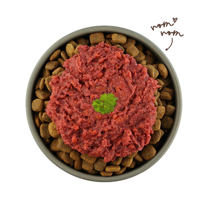 Miska s hnědými granulemi a červeným vlhkým krmivem, ozdobená lístkem petržele. Ručně psaný text: 'nom nom'.