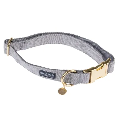 Nomad Tales dog collar in grey with gold buckle and pendant. Woven pattern, brand label visible.