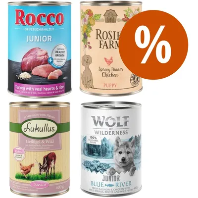 Quattro lattine di cibo umido per cuccioli: Rocco Junior, Rosie's Farm Puppy, Lukullus Junior, Wolf of Wilderness Junior Blue River. Simbolo percentuale arancione indica offerta o sconto.