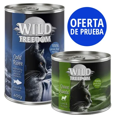 Dos latas de Wild Freedom para gatos: Cold River (pollock y pollo, 400 g) y Green Lands (cordero y pollo). Texto visible: '100% grain-free recipe'. Círculo azul: OFERTA DE PRUEBA.