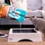 Sanicat Clumping cat litter is poured into a wooden cat toilet while a grey cat stands next to it.