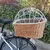 Panier en osier avec grille métallique blanche et doublure à pois, fixé sur le porte-bagages arrière d’un vélo. Matériaux visibles : osier, métal, tissu.