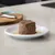 Portie natvoer op een wit bord, geserveerd met saus. Op de achtergrond een keukenwerkblad en een snijplank.
