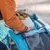 Person hilft einem kleinen Hund, in einen blauen Tiertransportwagen mit Netzfenster einzusteigen.