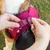 Red dog harness with click fastener being put on. Hands show how the fastener is closed.