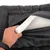 Main ouvrant une housse noire à fermeture éclair pour montrer un matelas en mousse blanche à l’intérieur, surface extérieure en tissu synthétique à petits points.