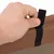 Close-up van een hand die een zwarte klittenbandsluiting op een bruine stof opent. Toont de functie van de sluiting.