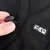 Nahaufnahme eines schwarzen Stoffes mit Kordelzug und Logo. Hand zeigt die Funktion des Kordelzugs.