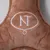 Braunes Plüschmaterial mit gesticktem weißen Logo 'NT' in einem ovalen Rahmen.