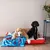 Two dogs lying on a colourful dog bed with blue-red design in a room with wooden floor and decoration.