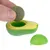 Jouet en forme d’avocat vert et jaune, une main tient une boule ronde verte à placer dans l’ouverture centrale du jouet. Coque en plastique démontée visible à côté.