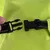 Gros plan sur une attache en plastique noir avec sangle textile noire, devant un tissu vert vif. Une main tient l’un des côtés de l’attache.