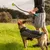 Dog with black coat and pattern looking at a ball launcher with yellow KONG ball, held by a person in sportswear on a lawn.