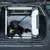 Hund in einer Transportbox aus Metall und Kunststoff im Kofferraum eines Autos, gesichert mit einem blauen Sicherheitsgurt.