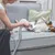 Persona usando un accesorio de aspiradora para eliminar pelo de mascota sobre un perro tumbado en un sofá gris.