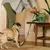A person removes a green dog waste bag roll from the 'Earth Rated Poop Bags, unscented, 120 count' packaging while a dog stands next to them.