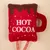 Red plush toy in the shape of a cup with brown chocolate glaze and white text 'HOT COCOA'.