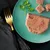 Close-up of pâté-style wet food on a green plate, garnished with parsley and a gold fork beside it.