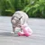 Graue Katze spielt mit einem rosa Plüsch-Flamingo auf einer Holzterrasse.