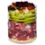 Glass container with visible layers of raw meat, green apple slices, celery, cherry tomatoes, beetroot pieces and small yellow grains at the bottom. All ingredients clearly separated.