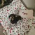 Cão sobre uma manta com motivos de Natal e uma almofada com bordado de cão. Produto mostra têxteis decorativos para animais de estimação.