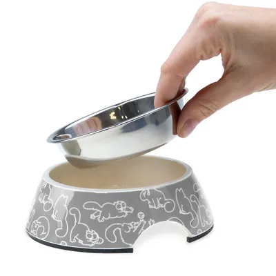 Hand lifts removable stainless steel bowl from grey feeding bowl with cat motifs.