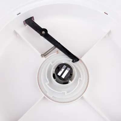 Close-up van een wit kunststof mechanisme met tandwiel en zwarte hendel, onderdeel van een automatische voerdispenser.
