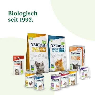 Ассортимент кормов для кошек Yarrah: сухие и влажные корма, паучи, лакомства. Видны надписи BIO, 100 %, Adult Cat Food, Paté Multipack. Текст на немецком: Biologisch seit 1992.