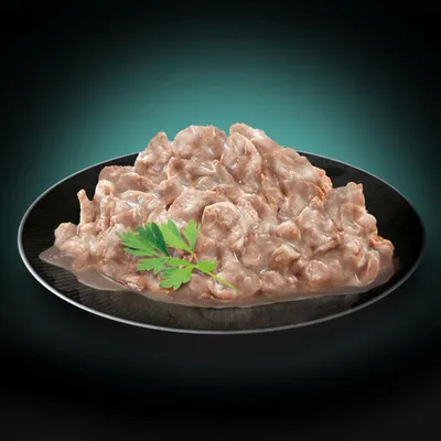 Κοντινή λήψη από τρυφερά κομμάτια κρέατος σε σάλτσα σε μαύρο πιάτο, διακοσμημένα με φρέσκο φύλλο μαϊντανού.