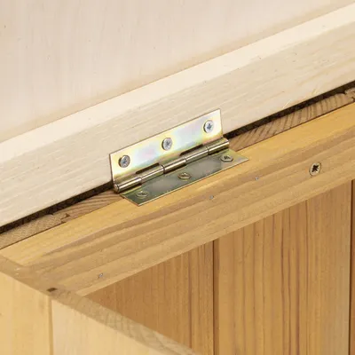 Primo piano di una cerniera in metallo fissata a una struttura in legno con viti.