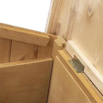 Detail drevenej konštrukcie s kovovým pántom, zobrazené spoje a hrany materiálu. Viditeľné prírodné drevo bez povrchovej úpravy.