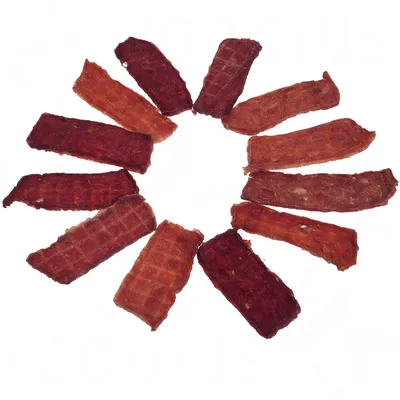 Kreisförmige Anordnung von getrockneten Fleischstreifen in verschiedenen Rottönen, geeignet als Snack oder Belohnung.