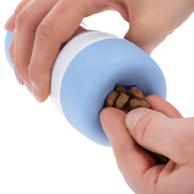 Hand befüllt ein blau-weisses Spielzeug mit Trockenfutter. Demonstration der Nutzung des Produkts.