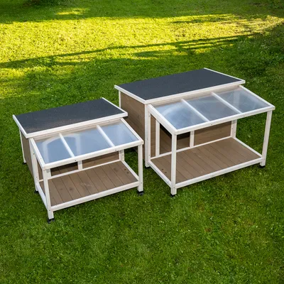 Deux abris extérieurs en bois avec toit plat noir et panneaux transparents inclinés, posés sur une pelouse. Un modèle petit et un modèle grand sont visibles côte à côte.