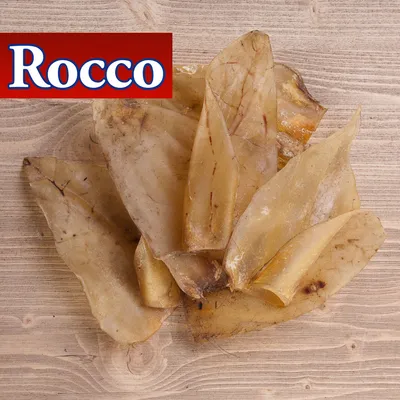 Rocco torkade hundsnacks, flera ljusbruna bitar på träyta. Varumärket Rocco synligt uppe till vänster.