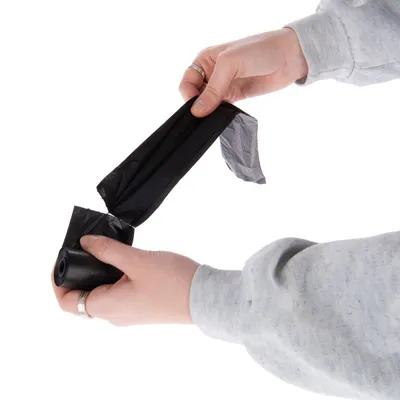 Handen scheuren een zwarte plastic zak van een rol af. Zichtbaar: gladde structuur, geen merknaam of tekst op de zakken.