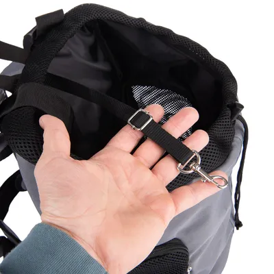Primo piano di uno zaino grigio con rete nera e cintura di sicurezza integrata con moschettone in metallo. Mano mostra il fissaggio della cintura.