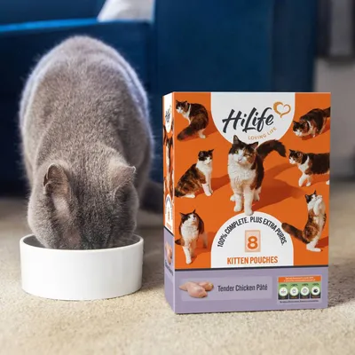 Box of HiLife Loving Life kitten pouches, tender chicken pâté flavour, 8 pack, shown next to a cat eating from a bowl.