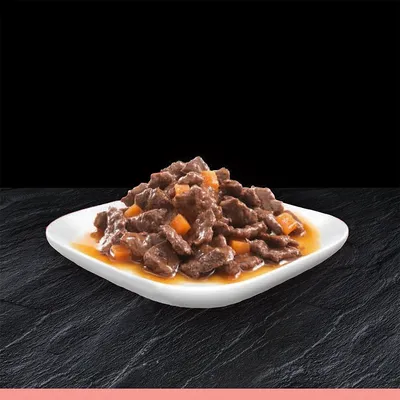 Primo piano di pezzi di carne in salsa con verdure su un piatto bianco, presentato su sfondo nero.