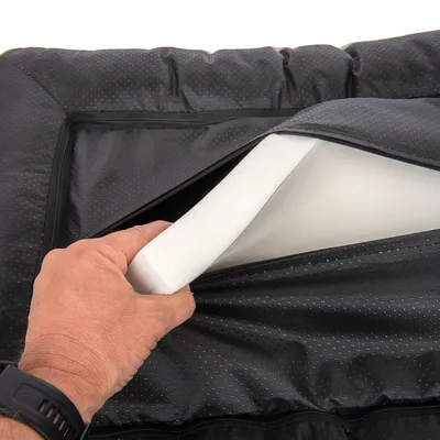 Main ouvrant une housse noire à fermeture éclair pour montrer un matelas en mousse blanche à l’intérieur, surface extérieure en tissu synthétique à petits points.