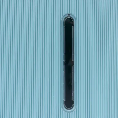 Nahaufnahme eines vertikalen Sichtfensters aus transparentem Kunststoff auf einer gerippten, hellblauen Oberfläche.