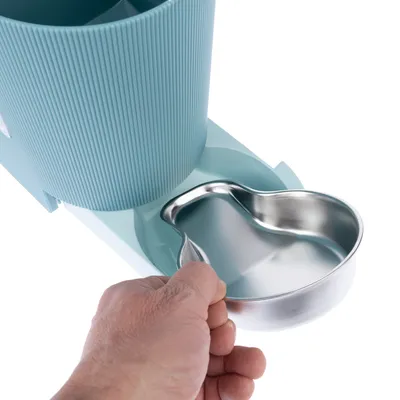 Hand hält eine Edelstahlschale, die aus einem blauen Futterspender entnommen wird. Zeigt Funktion des Spenders mit herausnehmbarer Schale.