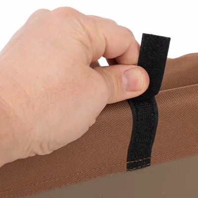 Close-up van een hand die een zwarte klittenbandsluiting op een bruine stof opent. Toont de functie van de sluiting.