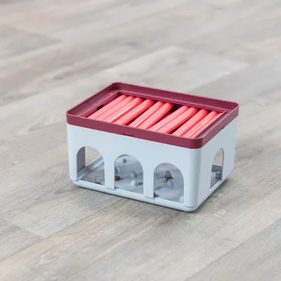 Plastová interaktivní hračka pro domácí mazlíčky s červenými posuvnými tyčemi a otvory po stranách, uvnitř viditelné malé pamlsky.