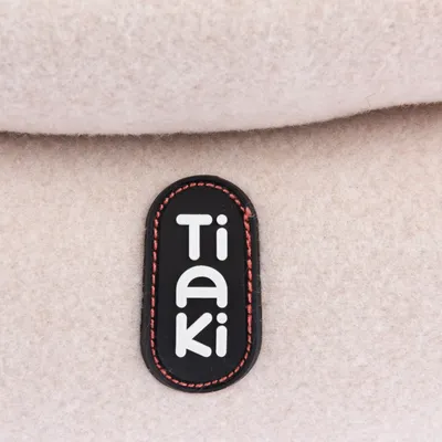 Tiaki. Merkenlogo op beige stof met zwart label en rode naad.