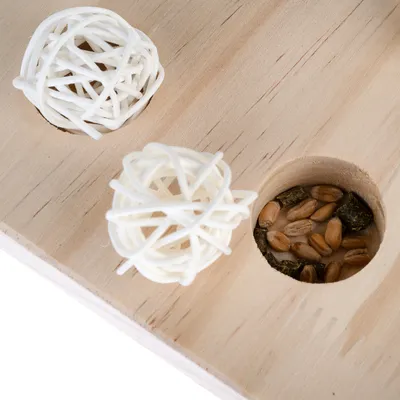 Drewniana zabawka z dwoma wgłębieniami: jedno zawiera białe piłki z kratką, drugie ziarna i kawałki karmy. Wspiera aktywność i interakcję.