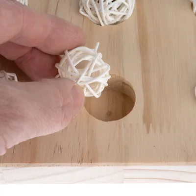 Ręka wkłada biały rattanowy piłkę do wgłębienia drewnianej zabawki.