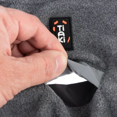 Hand öffnet eine graue Tasche mit reflektierendem Streifen, Tiaki-Label sichtbar auf dem Stoff.