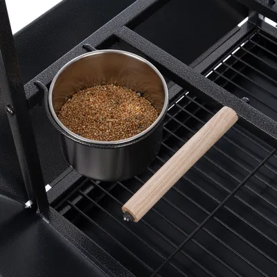 Metallschale mit Vogelfutter, platziert auf einem schwarzen Gitterrost mit Holzgriff.