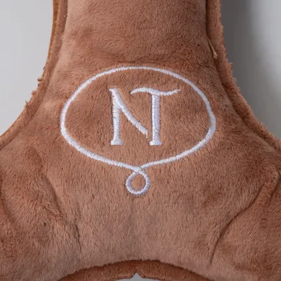 Braunes Plüschmaterial mit gesticktem weißen Logo 'NT' in einem ovalen Rahmen.